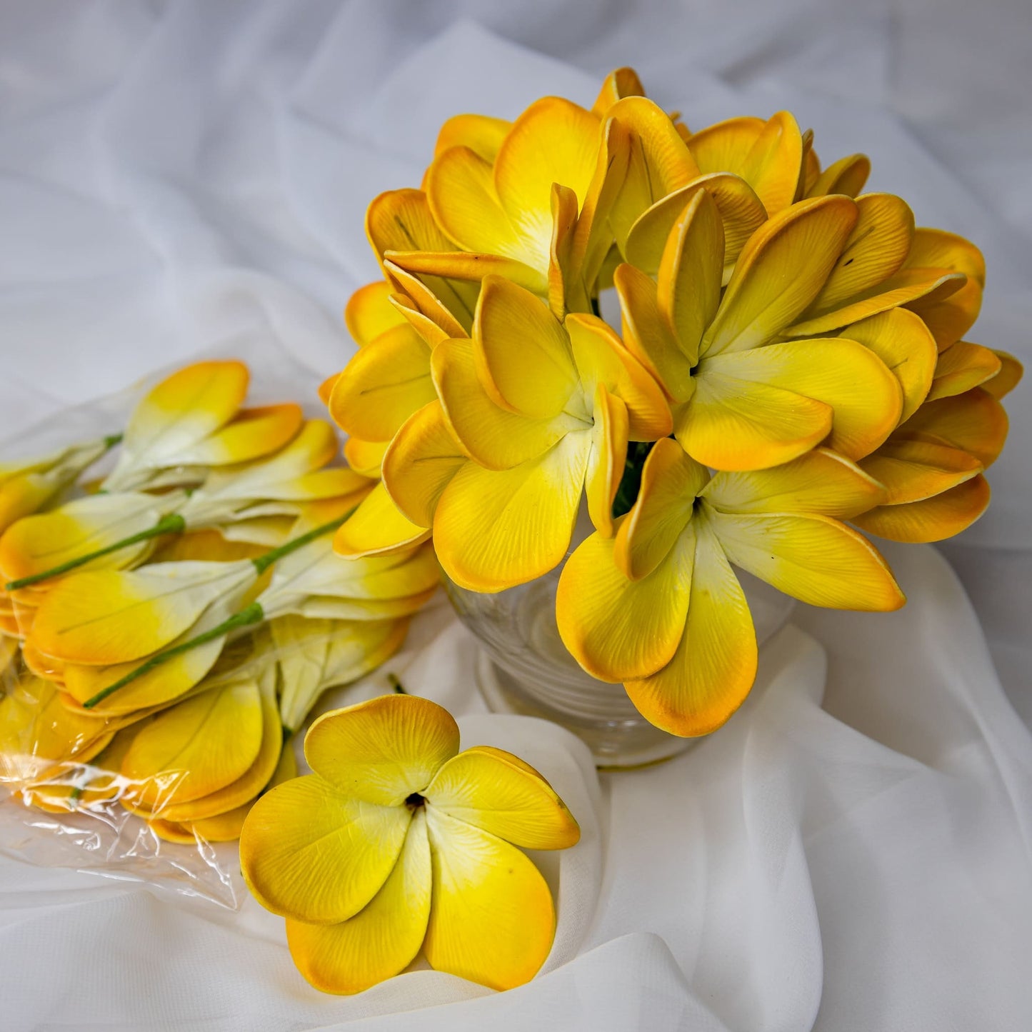 artificial tahitian gold frangipani flowers placed in transparent glass vase