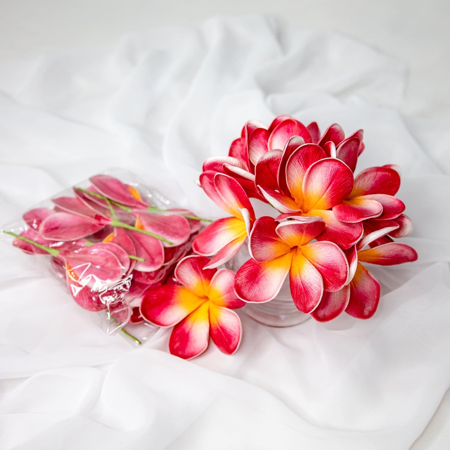 artificial red orange frangipani flowers placed in transparent glass vase