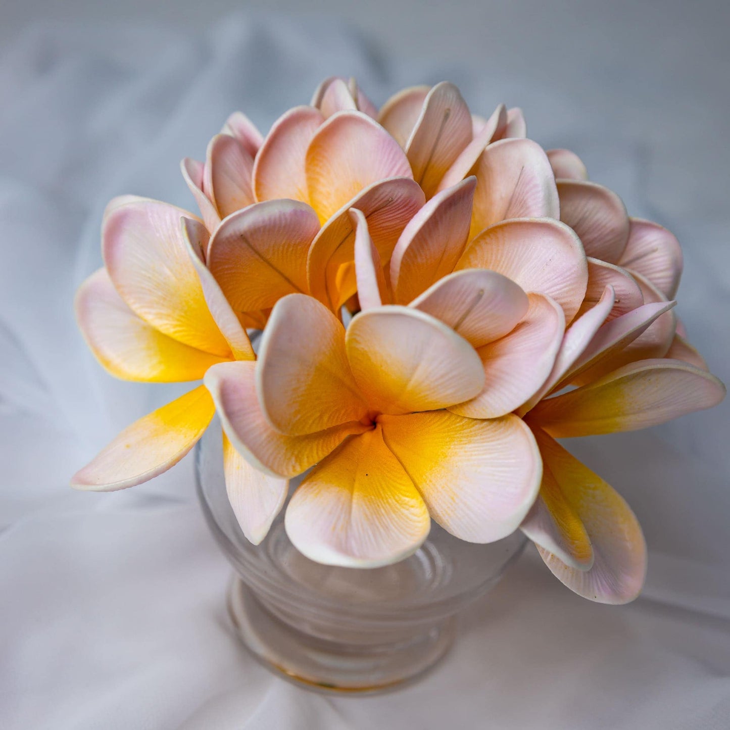 artificial pale frangipani flowers place in transparent glass vase