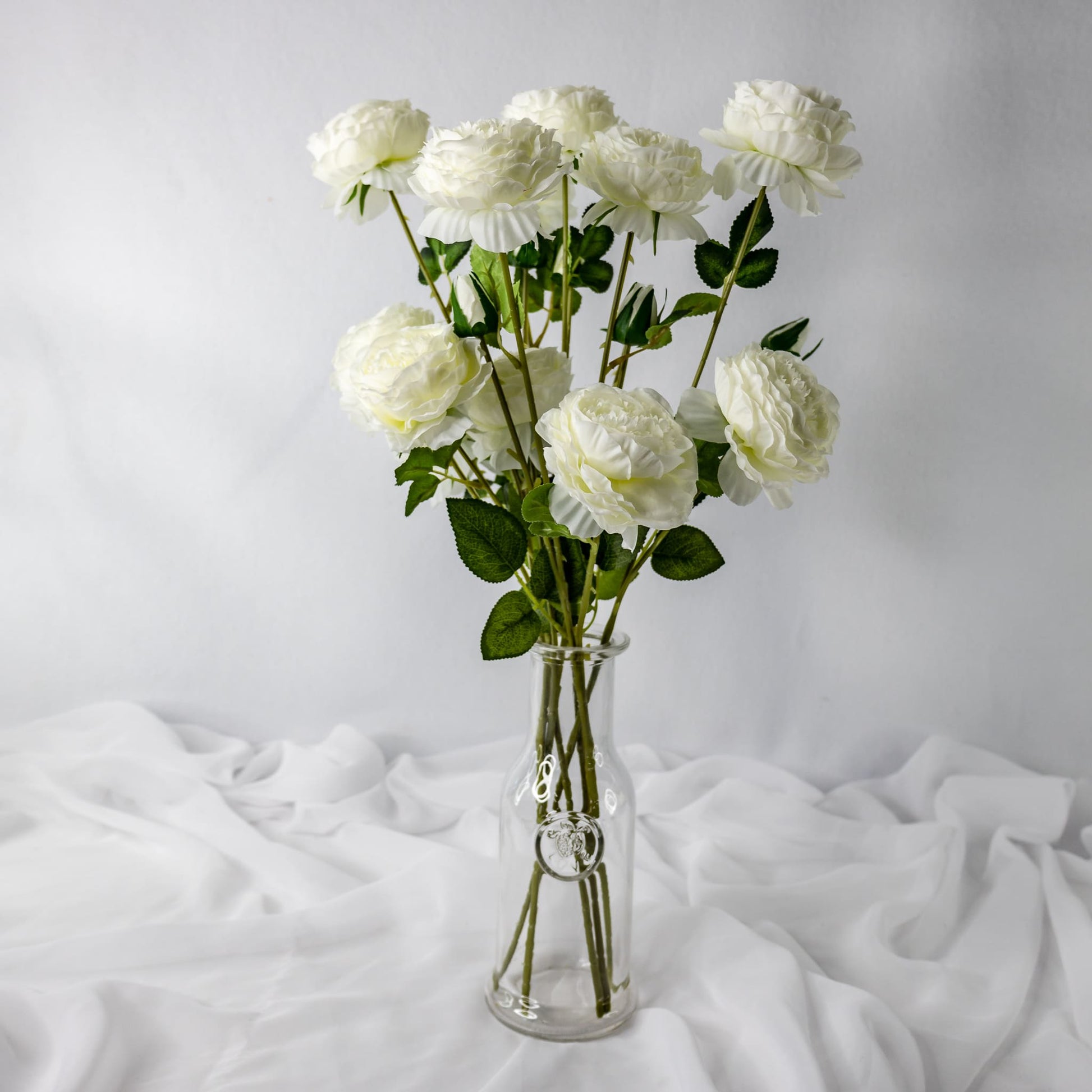 artificial white mini peonies placed in transparent glass vase