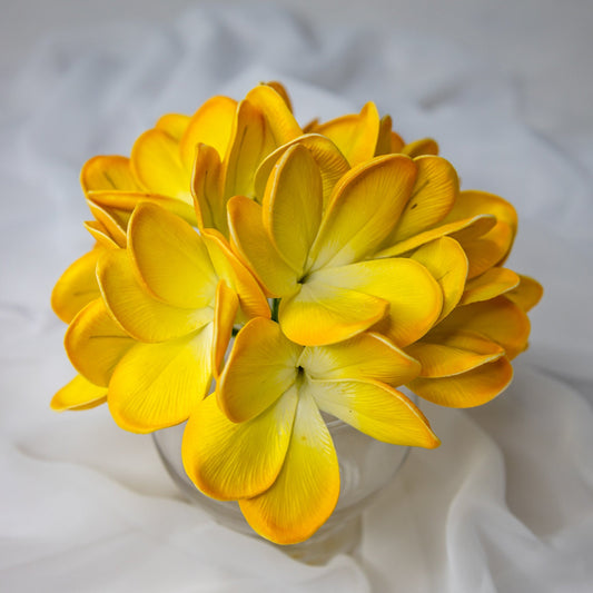 artificial tahitian gold frangipani flowers placed in transparent glass vase top view